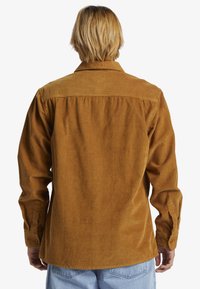 Brun corduroy skjorte med vertikale striber, lange ærmer, knaplukninger ved håndleddene og en yoke-detalje på ryggen, med en afslappet pasform.