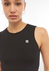 Top negro sin mangas hecho de una tela suave, con un cuello redondo y un pequeño parche de logo en el lado izquierdo.