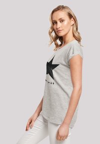 Gray cotton T-shirt with a black star graphic. Short sleeves, round neckline, and a relaxed fit. Paired with white pants.