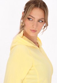 Felpa gialla con zip in morbido materiale felpato e cappuccio. Caratterizzata da un design aderente e una texture sottile, offre un look casual e confortevole.
