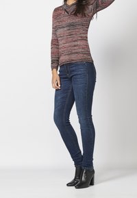 Pull en maille à rayures rouges et noires avec manches longues, associé à un jean skinny en denim bleu et des bottines à talons noires.
