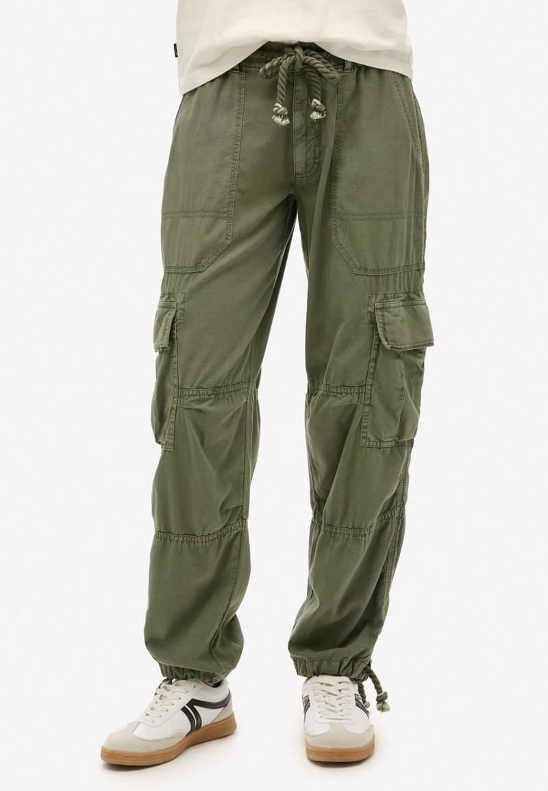 Pantalons cargo en coton vert olive, dotés d'une taille élastique avec cordon de serrage, de plusieurs grandes poches et de jambes fuselées. Une paire de baskets en dessous.