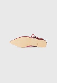 Chaussure plate rouge avec un bout pointu et une tige en daim texturé, dotée d'un détail en nœud et d'une semelle extérieure de couleur claire.
