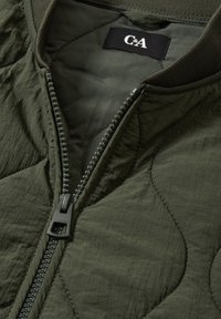 Quilted green bomber jacket with a zip closure, ribbed collar, and smooth texture. Features an internal label at the neck.