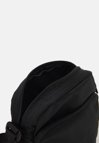 Borsa nera con finitura testurizzata, caratterizzata da una cerniera superiore e un design compatto. Interno foderato, con dettagli di cucitura visibili.