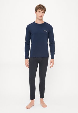 Marineblauses Shirt mit Logo auf der Brust und schwarzen, enganliegenden Hosen. Glatter, elastischer Stoff, körperbetontes Design und Rundhalsausschnitt.