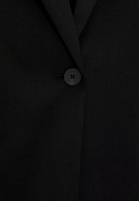 Tissu noir avec un seul bouton noir fermé au centre, doté d'un col à revers cranté.