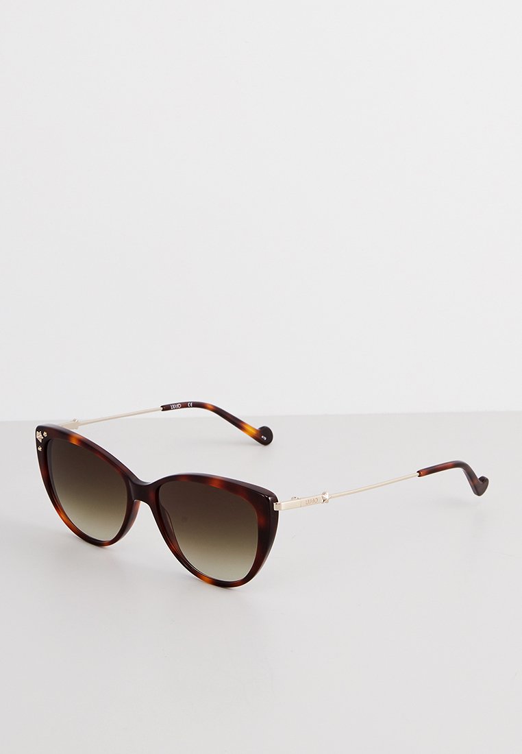 Lunettes de soleil cat-eye en écaille de tortue brune avec des verres sombres dégradés et des branches en métal doré fines sur une surface blanche.
