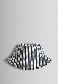 Prúžkovaný klobúk typu bucket vyrobený z bavlny. Má striedavé námornícke modré a biele vertikálne pruhy, široký mäkký krempa a prešité švy.