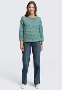 Striped long-sleeve top in teal and white, paired with blue jeans and white sneakers. The top features a boat neckline and relaxed fit.