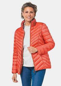 Padded orange jacket mit einem Reißverschluss, Chevron-Steppmuster, Stehkragen und leichtem Material. Über einem weißen Hemd getragen.