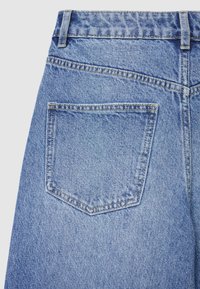 Jeans in denim azzurro chiaro con una tasca posteriore. Il tessuto ha una texture sottile, con cuciture visibili intorno alla tasca e alla vita.