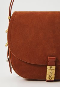 Bruine suède handtas met een afgeronde flap, gouden hardware-accenten en een gebrandmerkte sluiting. Soepele textuur en gestructureerde vorm.