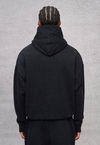Sudadera corta negra hecha de material rico en algodón, con mangas largas, una gran capucha y un diseño simple y minimalista.
