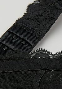 Černé spodní prádlo s krajkovým zdobením, texturovanou tkaninou a nastavitelnými ramínky. Obsahuje zapínání na háček a oko, složité vzory květinové krajky.