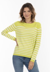 Maglione a righe giallo brillante con strisce orizzontali bianche, colletto a girocollo, maniche lunghe e vestibilità rilassata, abbinato a jeans in denim.