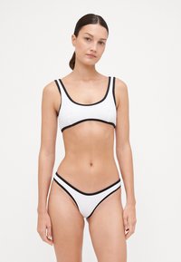 Fehér bikini szett texturált anyaggal, fekete kiemelésekkel. A felső része kerek nyakkivágású és széles pántokkal rendelkezik; az alsó része alacsony ülepű.