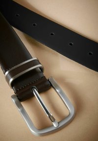 Cinturón de piel marrón con hebilla de metal plateado. Presenta una textura suave y múltiples agujeros de ajuste en la parte inferior negra.
