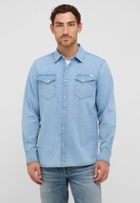 Jasnoniebieska koszula dżinsowa z długimi rękawami, z dwoma kieszeniami na piersi i zapięciem na guziki, w połączeniu z jasnoniebieskimi dżinsami.