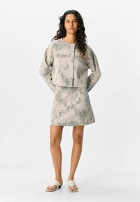 Ensemble en tissu gris clair avec imprimé floral ; comprend un haut court et une jupe assortie. Les sandales présentent un design à brides croisées.