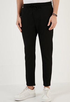 Sorte ribbede bukser med elastisk talje og snor. Tætsiddende design, der slutter ved anklerne, parret med hvide sneakers.