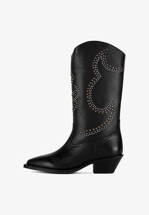 Czarny kowbojski but ze skóry, z zaostrzonym noskiem i korkowym obcasem. Ozdobiony metalowymi ćwiekami ułożonymi w zakrzywione wzory na cholewce.