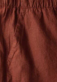 Tessuto color ruggine con una texture morbida, dotato di una vita elasticizzata e di una tasca laterale, che mette in risalto il materiale e la finitura simili a lino.