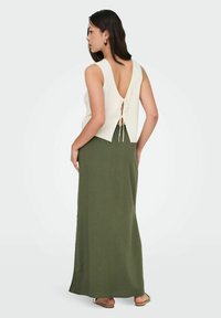 Witte geribbelde top met een diepe V-rug en strikdetail, gecombineerd met een olijfgroene lange rok. Beide kledingstukken hebben een gladde textuur.