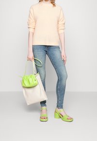 Světle broskvový svetr, modré úzké džíny, zelené silné sandály a dvoubarevná taška s akcentem v podobě zeleného stahovacího pytlíku.