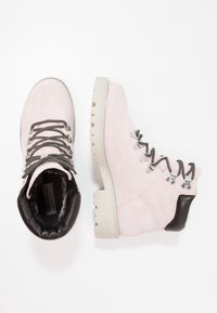 Botas de tobillo de ante rosa claro con un cuello acolchado negro, cordones grises y una suela gruesa beige. Presentan ojales plateados y un forro suave.