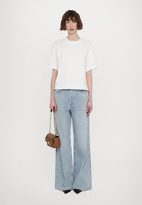 T-shirt bianco a maniche corte abbinato a jeans ampi blu chiaro. Una piccola borsa marrone con tracolla dorata è tenuta in una mano.