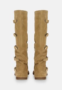 Par de botas altas de ante marrón claro con cinco correas laterales ajustables y tacones bajos de madera, mostradas desde atrás sobre fondo blanco.