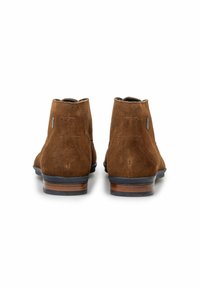 Bottines en daim marron avec une finition lisse, un bout arrondi, des coutures décoratives et des accents en bois au niveau du talon. La vue de l'arrière montre un design échancré.