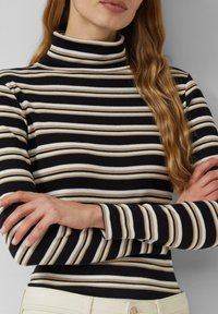 Czarny golf w poziome paski w kolorze kremowym i beżowym. Dopasowany, prążkowany, z długimi rękawami i wysokim kołnierzem.