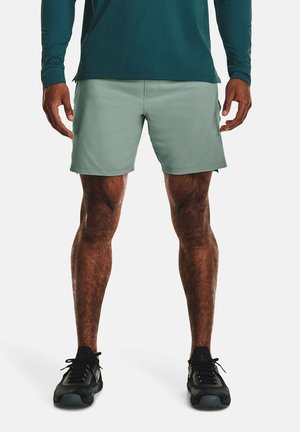 Hellgrüne Sportshorts aus weichem Stoff, mittellang bis zur Mitte des Oberschenkels, kombiniert mit schwarzen Sportschuhen mit Mesh-Akzenten und profilierten Sohlen.