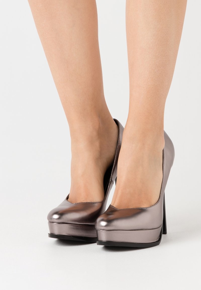 Talons compensés avec une finition bronze métallique, bout arrondi et une texture élégante et brillante. Talon haut et mince avec une silhouette lisse.