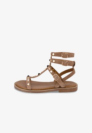 Sandales gladiateur en daim marron avec trois brides de cheville réglables, ferrures dorées et perles décoratives. Semelle plate avec détail cousu.