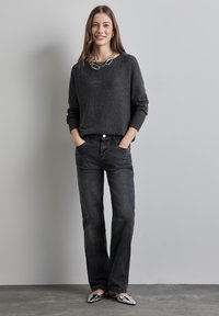 Maglione grigio scuro con polsini a coste, abbinato a jeans neri e scarpe basse metalliche. Una semplice collana a catena aggiunge contrasto.