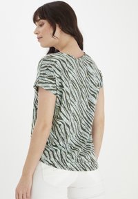 Zebra raksta īsām piedurknēm augšdaļa zaļā un gaiši zilā krāsā ar noapaļotu kakla izgriezumu un mīkstu audumu ar vieglu tekstūru.