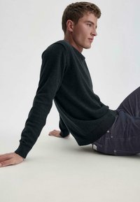 Zwarte trui met een ronde halslijn, slim fit en lange mouwen, gecombineerd met donkere jeans. Gladde textuur, geen zichtbare patronen of logo's.