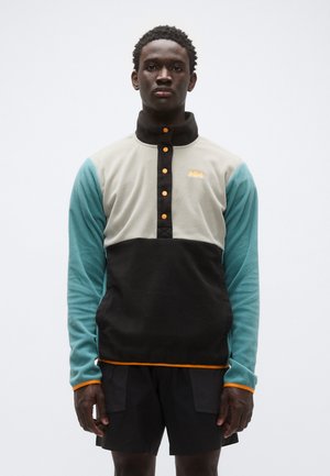 Fliisist pullover kõrge kraega, millel on beež, must ja türkiissinine värv, oranžid detailid ning ees kinnitusnupud.