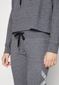 Šedý svetr s krátkým střihem a žebrovaným lemem, doplněný o šedé tepláky se stejným vzorem, s černým šňůrkováním a stříbrným vzorem.