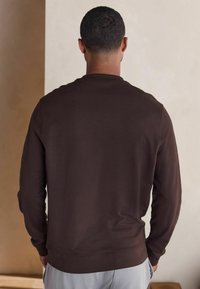 Pruun pikkade varrukatega sviiter ümmarguse kaelusega ja ribidega mansettidega. Sile tekstuur, keharikka disain ja ei mingeid nähtavaid mustreid ega aktsente.