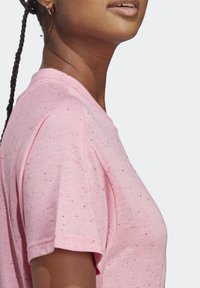 Vaaleanpunainen, lyhythihainen t-paita pehmeästä kankaasta, jossa on pilkullinen kuvio pienillä monivärisillä täplillä. Pyöreä pääntie, rento istuvuus.