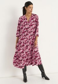 Lange, gelaagde jurk gemaakt van een lichtgewicht stof met een roze bloemenpatroon op een bordeauxrode achtergrond; diepe V-halslijn, 3/4 mouwen.