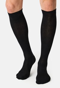 Knælange sorte sokker lavet af ribbet materiale med en glat tekstur. Har et tætsiddende design uden synlig branding eller mønstre.