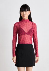 Dlhý rukáv, priesvitný top v ružovej farbe s motívom usmievajúcich sa tvárí, skombinovaný s čiernou obtiahnutou sukňou. Vysoký golier s designom do V.