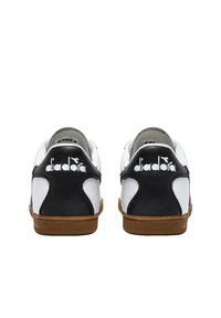 Scarpe sportive in pelle bianca e nera con suola in gomma, caratterizzate da accenti diagonali e logo in rilievo sul tallone.