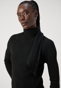 Mustad ribakudumine turtleneck-sviiter, millel on ainulaadne õlavarre drapeering, tekstuuriga viimistlus ja keha lähedane disain.