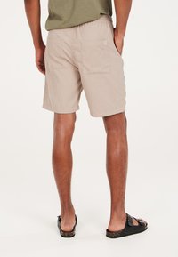 Pantaloni shorts beige chiaro realizzati in un tessuto testurizzato, con vita elastica e due tasche posteriori. Abbinati a sandali neri. Design pulito e minimalista.